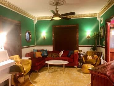 Cozy living room with green walls, stylish furniture, and a decorative ceiling fan.