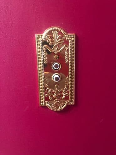 Vintage gold doorbell plate on a red wall with ornate design.