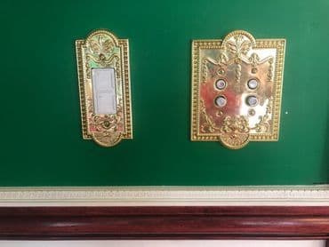 Decorative gold light switches on a green wall, showcasing intricate design details.