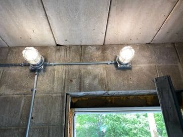 Industrial ceiling lights mounted on concrete walls, illuminating a workspace with natural light.