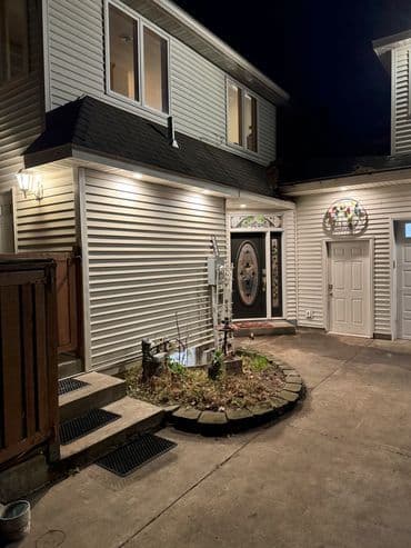 Well-lit entrance of a modern house with landscaped garden at night.