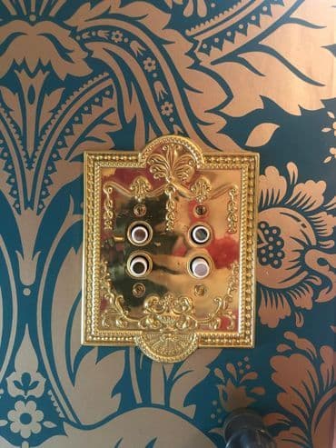 Elegant gold wall switch plate with decorative patterns on teal background.