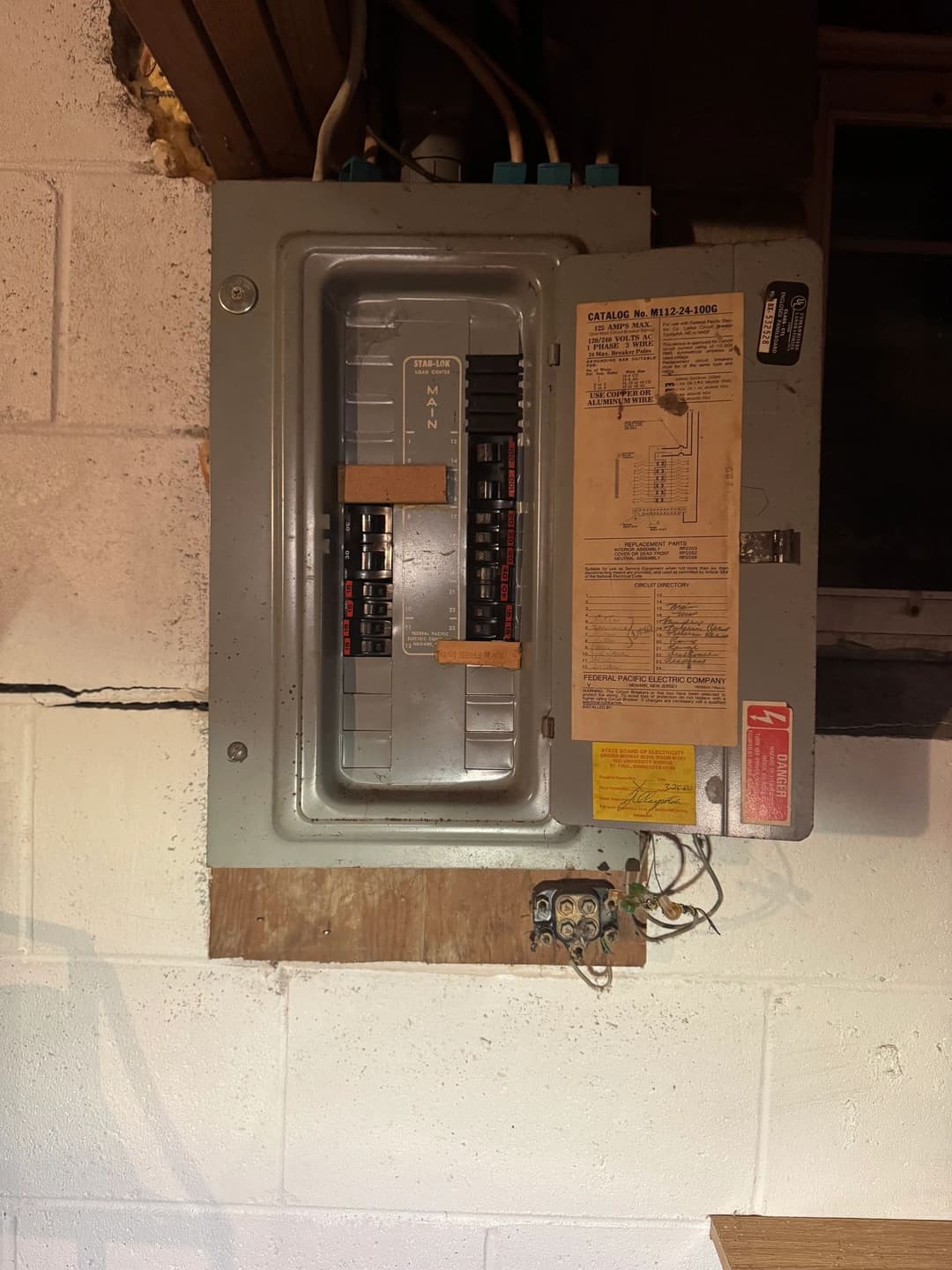 Electrical panel with circuit breakers mounted on a wall in a basement setting.