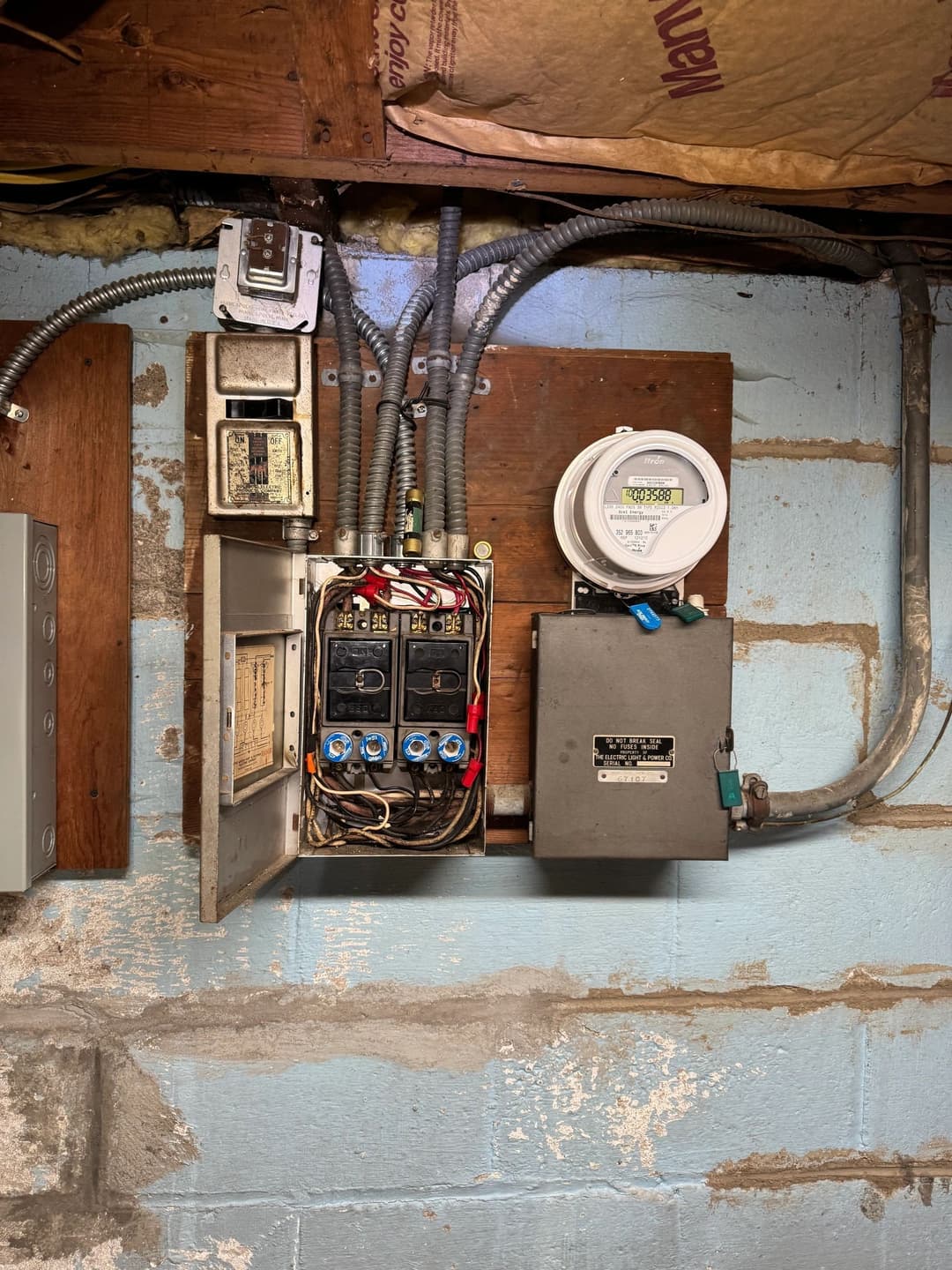 Electrical panel and smart meter installation in a basement with wiring and circuit breakers.
